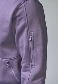 Felpa di cotone viola con tasca con zip sulla manica sinistra e una toppa texturizzata vicino alla spalla. Finitura liscia, design casual.