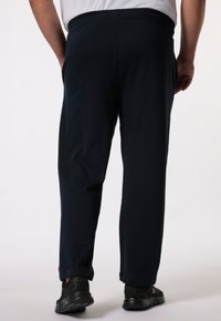 Pantalones de chándal navy con una cinturilla elástica y bolsillos laterales, con una textura suave y piernas ajustadas, combinados con zapatillas deportivas negras.
