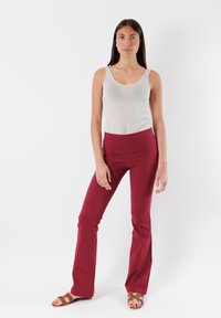 Top in cotone grigio a scollo rotondo e pantaloni a zampa d'elefante bordeaux a vita alta, abbinati a sandali marroni con zeppa su uno sfondo bianco uniforme.