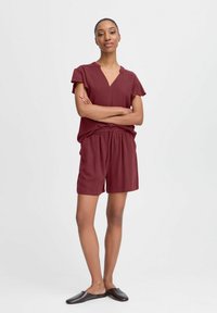 Ensemble bordeaux en deux pièces comprenant un haut à manches courtes avec un col en V et un short à taille élastique. Tissu texturé avec poches latérales.