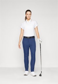 Balta polo marškinėliai su trumpomis rankovėmis ir apykakle, tamsiai mėlynos kelnės, juodas diržas ir balti sportbačiai. Dešinėje rankoje laiko golfą.