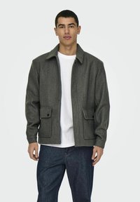 Grijze wollen jas met een kraag, twee voorzakken en drukknoopsluitingen. Draag het over een wit shirt en combineer het met donkerblauwe jeans.