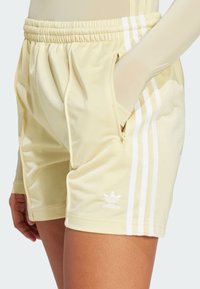Geel sportieve shorts van gladde stof met een elastische tailleband, zijzakken en drie witte verticale strepen. Adidas-logo weergegeven.
