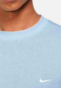 Ljusblå bomullströja med rund halsringning som har en vit Nike-logga på vänster sida av bröstet. Mjuk textur med standard passform.