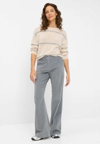 Lichtgrijze, flared corduroypantalon met een gladde textuur en voorzakken. Gecombineerd met een beige trui met horizontale strepen.