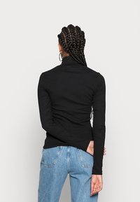 Schwarzes langärmliges Rollkragenoberteil mit taillierter Passform, glatter Textur und Rückennahtdetails, kombiniert mit hellblauen Denim-Jeans.