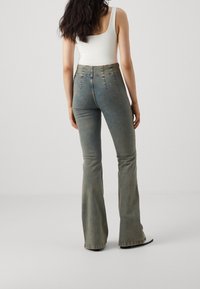 Höga, blå utsvängda jeans med en urtvättad finish, med knäppning fram, sydda detaljer och en figursydd silhuett.