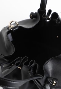 Musta nahkainen ämpärilaukku, jossa on pehmeä tekstuuri, rypyttyneet yläreunat, kultaiset yksityiskohdat ja tilava sisustus.