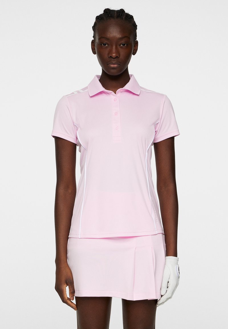 Rosa polo skjorta med krage, korta ärmar och knappslå. Har vita detaljer och en veckad kjol. Bärs med en vit handske.