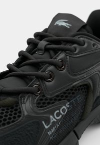 Chaussure de sport noire en matériaux mesh et synthétiques, avec des lacets ronds, des œillets métalliques et un logo sur la languette.