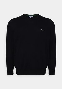 Pull noir à col rond en tissu texturé, avec un petit logo vert brodé sur la poitrine gauche et des poignets et ourlet côtelés.