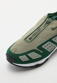 Nike avalynė žaliai ir smėlio spalvos su užtrauktuku, su tekstūruotais akcentais ir perforuotomis dalimis šonuose, užtikrinančiomis pralaidumą orui.