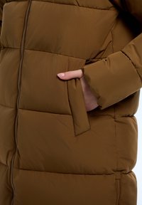 Bruine pufferjack met een ritsluiting, horizontaal gestikte patroon en een zijzak met een flap. Glad, lichtgewicht stof.