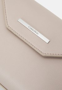 Clutch in pelle beige di Calvin Klein con una superficie liscia, patta inclinata, placca logo in tonalità argento e dettagli di cucitura a contrasto.