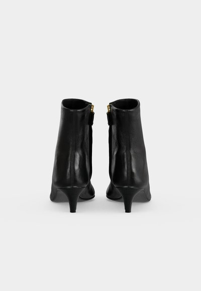 Paire de bottines en cuir noir avec petits talons, vues de dos sur un fond clair uni.