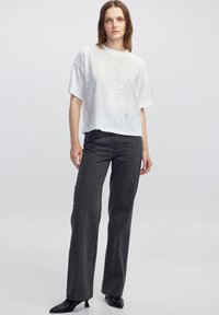 Witte cropped t-shirt van textiel met structuur, gecombineerd met hooggeknoopte donkergrijze jeans en zwarte puntige hakken. Eenvoudig, strak ontwerp.