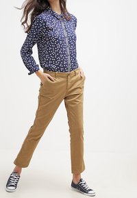 Chemise bleu marine à pois avec col et boutons, chinos kaki, et baskets bleu marine. La chemise comporte des pois de couleur claire et une fermeture éclair à l'avant.