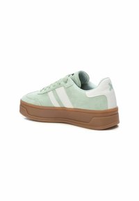 Zapatilla de ante verde con rayas blancas, puntera redonda y suela de goma marrón. Presenta un tobillo acolchado y acentos en contraste en el talón.