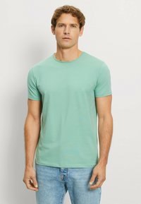 Mint green short-sleeve t-shirt made of soft cotton fabric, featuring a round neckline and a slim fit. Paired with light blue jeans.