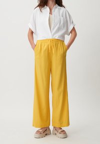 Witte short-sleeve button-up shirt en gele wijde broek van lichtgewicht stof, met een elastische taille en trekkoorddetails.