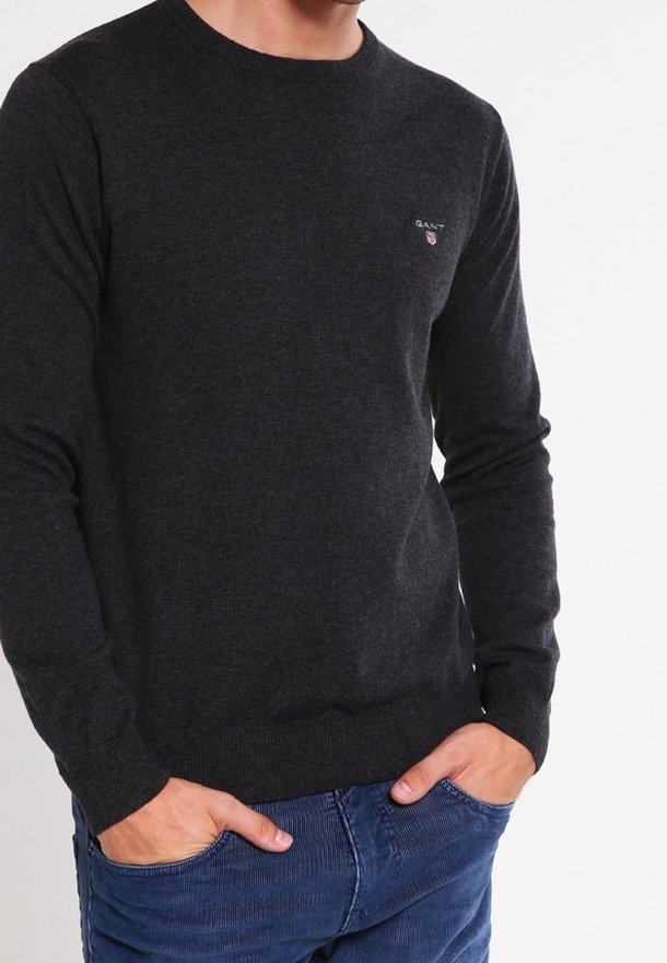 Maglione lavorato a maglia grigio scuro con maniche lunghe, polsini e orlo a costine, con un piccolo logo sul petto. Abbinato a jeans blu.