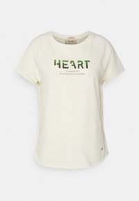 Krémové tričko z měkké tkaniny, s kulatým výstřihem, krátkými rukávy a potištěným slovem "HEART" v zelené barvě s dalším textem pod ním.