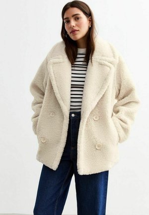 Crème faux fur jas met een dubbelbreasted ontwerp, brede revers en grote knopen, gecombineerd met een gestreept shirt en donkere spijkerbroeken.
