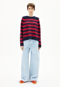 Navy- und rotgestreifter Pullover mit Rundhalsausschnitt, kombiniert mit weit geschnittenen hellblauen Jeans und orangenen Schuhen. Glatte Textur und lässige Passform.