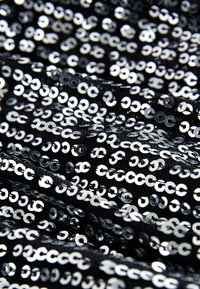 Tessuto nero ricoperto da paillettes argentate lucide, disposte in un motivo denso e sovrapposto, creando una superficie texturizzata e riflettente.