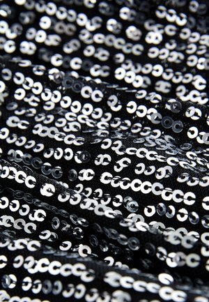 Sort stof dækket med skinnende sølvpalietter, arrangeret i et tæt, overlappende mønster, der skaber en tekstureret og reflekterende overflade.