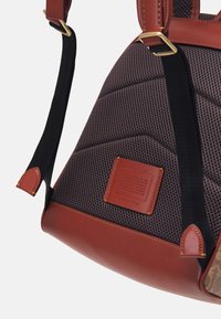 Brązowa torba skórzana i z siateczki o pikowanej fakturze, z akcentującymi paskami i jasnobrązową metką. Posiada złote okucia i ciemne uchwyty.