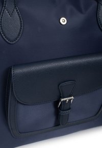 Borsa blu navy con un esterno in tessuto liscio, tasca in pelle texturizzata e hardware in metallo argentato per una chiusura sicura.