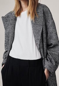Zwart-wit gemusterde oversized blazer over een wit T-shirt, gecombineerd met zwarte op maat gemaakte broeken. Zacht, gestructureerd materiaal.