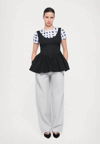 Top peplum negru cu mâneci scurte tie-dye, purtat cu pantaloni largi gri deschis și balerini negri ascuțiți. Design simplu și curat.