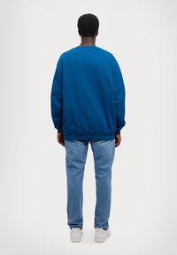 Blue sweatshirt with a crew neckline, oversized fit, and ribbed cuffs, paired with light blue jeans and white sneakers.