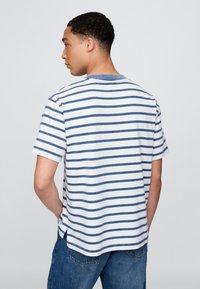Kortermet bomulls-T-skjorte med blå og hvite horisontale striper, rund hals, avrundet kant og splittdetaljer på sidene.
