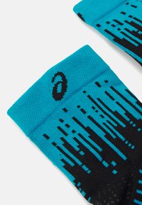 Türkise Sportsohlen mit schwarzem Digitalmuster, gerippten Bündchen und einem Markenlogo. Hergestellt aus atmungsaktivem Material für Komfort.