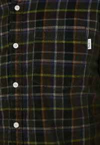 Kariertes Hemd in Dunkelgrün mit weißen Knöpfen, einer Brusttasche und Streifen in Blau, Orange und Gelb auf einem strukturierten Stoff.