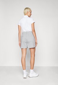 Camisa polo blanca y pantalones cortos de cuadro de gingham gris, con una cintura alta, bolsillos traseros y un corte relajado. Llevado con zapatillas deportivas blancas.