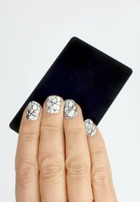 Schwarze Kreditkarte, die in der Hand mit kurzen, abgerundeten Nägeln gehalten wird. Die Nägel sind weiß mit schwarzen, abstrakten Linienmustern und einer matten Textur.