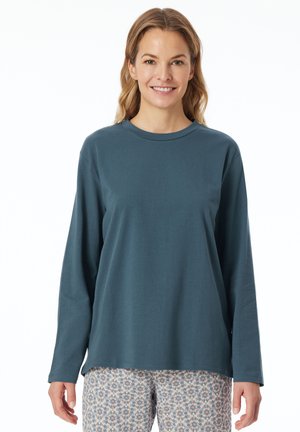 Langärmliges Oberteil mit Rundhalsausschnitt aus dunkelblauem Stoff, mit entspannter Passform. Kombiniert mit gemusterten Hosen in hellen Farben. Glatte Textur.