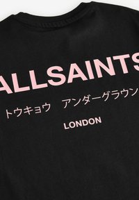 Juodas medvilninis marškinėlis su drąsiais rožiniais užrašais, kuriuose yra anglų ir japonų ženklai, įskaitant "ALLSAINTS" ir "LONDON" ant priekio.