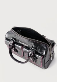 Μαύρη υφασμάτινη τσάντα με ροζ ραφές, δύο εμπρόσθιες τσέπες με πόρπες, λαβές στο πάνω μέρος και φερμουάρ μερικώς ανοιχτό που αποκαλύπτει το εσωτερικό.