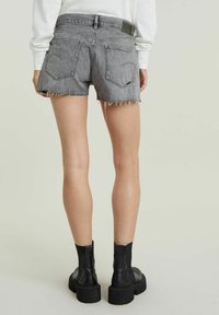 Harmaat farkkushortsit, joissa on revitty helma, kaksi takataskua ja kudottu etiketti vyötäröllä, yhdistettynä mustiin nilkkabootseihin.