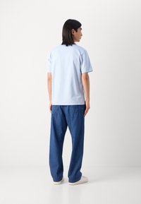 Light blue short-sleeve t-shirt paired with loose-fitting dark blue denim pants. Features a clean design and relaxed silhouette.