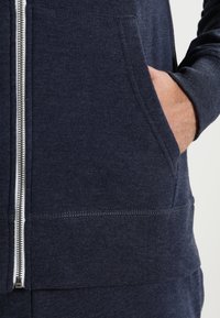 Sudadera con cremallera en color navy, fabricada en tejido suave, que cuenta con una cremallera frontal, bolsillos laterales y ribetes en los puños y el dobladillo. Textura suave con un diseño duradero.
