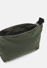 Borsa cosmetica in nylon verde con chiusura a zip, caratterizzata da una texture liscia e una maniglia laterale. Logo ricamato su un lato.