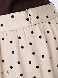 Jupe beige à pois noirs avec une fermeture éclair fermée au dos, portée avec un top en maille marron foncé.