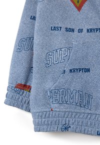 Giacca in denim blu con testo stampato "Superman" e "Ultimo Figlio di Krypton." Presenta polsini elastici e accenti decorativi in rosso e giallo.