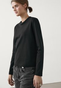 Black long-sleeve top made of soft fabric with a crew neck. Paired with dark gray jeans, featuring a simple, minimalistic design.